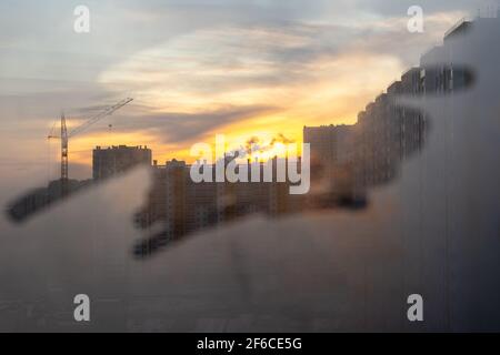 Geschäfts- und Designkonzept. Ein Blick durch ein nebelartiges Fenster auf eine Stadt im Bau, Wolkenkratzer, einen Baukran, eine neue Stadt, beleuchtet b Stockfoto