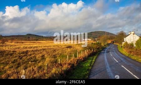 Die A762 in Mossdale in Dumfries und Galloway an einem sonnigen Wintertag, mit Bennan Hill und dem Galloway Forest Park im Hintergrund, Schottland Stockfoto