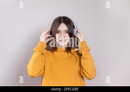 Ein Teenager-Mädchen mit langen dunklen Haaren lächelt und lacht in einem leuchtend orangefarbenen Hoodie mit Kopfhörern und hört Musik. Mit Platz für Text und Kopierraum Stockfoto