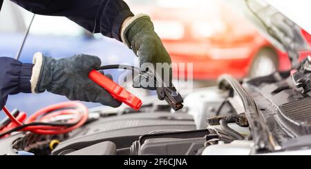 Menschliche Hände mit Überbrückungskabel über dem Automotor in Nahaufnahme. Stockfoto