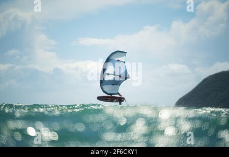 Ein Mann Flügel Folien auf dem Meer mit einem Hand gehalten aufblasbaren Flügel, Reiten ein Tragflächenboot Surfbrett. Türkisfarbenes Meer, wolkig blauer Himmel. Stockfoto