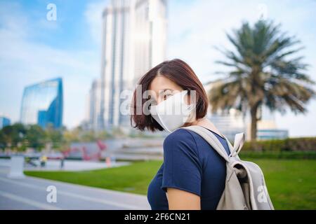 Porträt einer schönen Frau trägt eine Maske für verhindern Virus zu Fuß in Dubai mit Wolkenkratzern im Hintergrund. Genießen Reisen in United Arabian EM Stockfoto