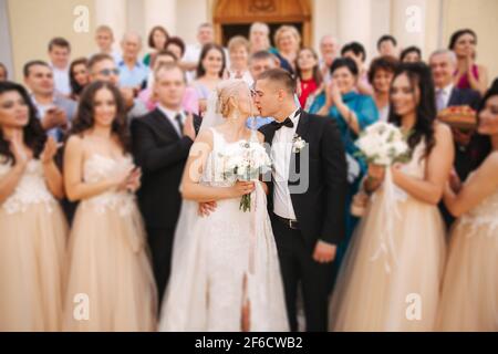 Bräutigam und Braut küssen sich von der Kirche. Frisch verheiratetes Paar am Sommertag Stockfoto
