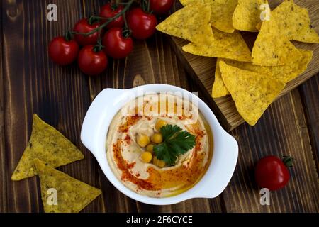 Hummus in der weißen Platte, Kirsche und Chips auf dem Holzhintergrund.Draufsicht. Stockfoto