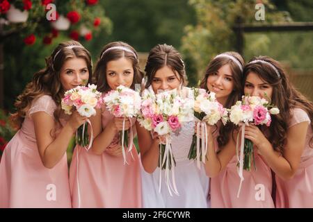 Glückliche Braut mit Brautjungfer halten Blumensträuße und haben Spaß draußen. Schöne Brautjungfer in gleichen Kleidern stehen von der charmanten Braut in langen Hochzeitskleid Stockfoto