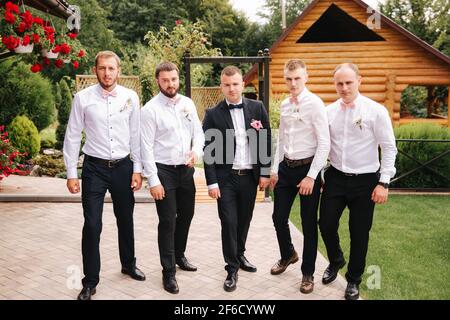 Stilvoller Groomsman mit dem Bräutigam, der auf dem Hinterhof steht und sich auf die Hochzeitszeremonie vorbereitet. Freund verbringt draußen Zeit miteinander Stockfoto