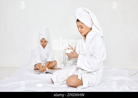 Mutter in weißen Bademänteln und Handtüchern Creme auf die Hände auftragen Stockfoto