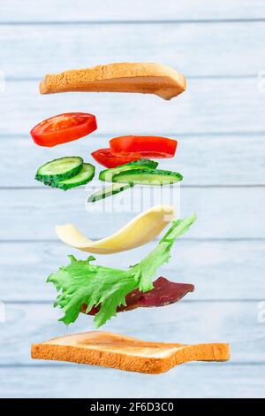 Fliegende Schichten von Sandwich mit Schinken, Käse und Gemüse auf dem Holzhintergrund. Frühstücksangebot Stockfoto