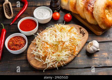 Verschiedene Saucen in Schüsseln auf einem Schneidebrettchen mit Knoblauch und geschreddertem Kohl und Tortillas. Auf dunklem rustikalem Hintergrund Stockfoto