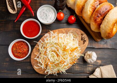 Verschiedene Saucen in Schüsseln auf einem Schneidebrettchen mit Knoblauch und geschreddertem Kohl und Tortillas. Auf dunklem rustikalem Hintergrund Stockfoto