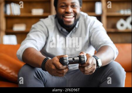 Fokus auf Joystick für Videospiele, schwarz aufgeregt Mann aus Fokus, sitzen auf Ledersofa, halten Joystick spielen Videospiele, entspannen an einem Wochenende, eine Pause von der Arbeit, allein zu Hause leben Stockfoto