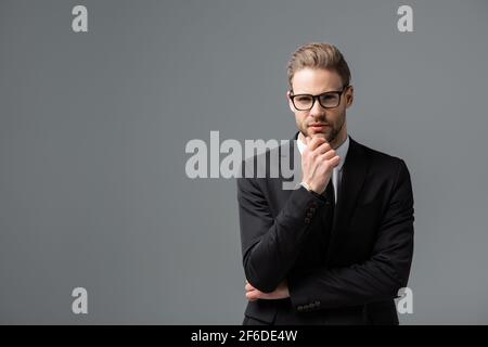 Ein nachdenklicher Geschäftsmann berührt das Kinn, während er die Kamera isoliert betrachtet Grau Stockfoto