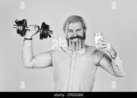 Quelle von Kalzium. Bärtiger Mann trinkt Milch. Trainieren Sie im Fitnessstudio. Milch gute Nährstoffe. Fettmenge. Vitamine für die Muskeln. Sportler halten Hantel und Stockfoto