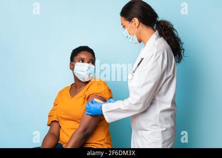 Medizinische Arbeiter, Die Schwarze Frau Mit Gesichtsmasken Impfen, Blauer Hintergrund Stockfoto