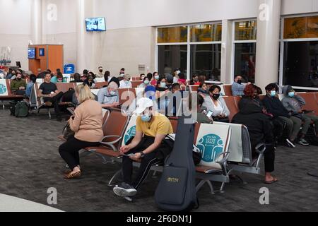 Menschen mit Gesichtsmasken sitzen zwischen physischen und sozialen Distanzierungszeichen mit den Worten „Stay Safe“. Platz lassen“ auf den Sitzen in Terminal B des Stockfoto