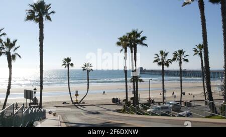Oceanside, California USA - 8 Feb 2020: Menschen, die spazieren gehen, Uferstraße des Resorts, tropischer Pazifikstrand mit Palmen. Person ridin Stockfoto
