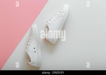 Weiße Sneakers, weibliche weiße Lederschuhe mit Schnürsenkeln auf rosa Hintergrund. Paar stilvolle Sneaker bequeme Sportswear Hipster Damenschuhe. Oben vi Stockfoto