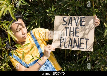 Porträt einer jungen Frau in der Natur mit einem Banner mit dem Text Save the Planet. Sie ist draußen. Stockfoto