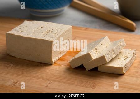 Stück frische rohe Bio-Tofu und Scheiben auf einem Schneidebrett aus nächster Nähe Stockfoto