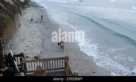 Encinitas, California USA - 21. Dez. 2019: Menschen, die nach dem Surfen am Strand spazieren, kaltes Meerwasser. Surfer in der Nähe von Meereswellen mit Surfbrett. Wasserspor Stockfoto