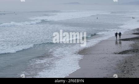 Encinitas, California USA - 21. Dez. 2019: Menschen, die nach dem Surfen am Strand spazieren, kaltes Meerwasser. Surfer in der Nähe von Meereswellen mit Surfbrett. Wasserspor Stockfoto