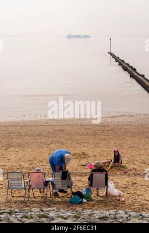 Southend on Sea, Essex, Großbritannien. März 2021. Der letzte Tag im März war heiß und hell in Southend, aber sehr trüb über der Themse-Mündung. Ein großes Containerschiff passiert Southend im nebligen Dunst, während eine Familie den Strand genießt Stockfoto