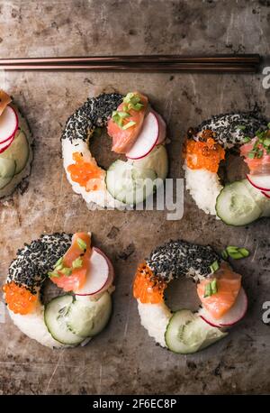 Sushi-Donuts mit Lachs, Gurke und Rettich auf dunklem Hintergrund, Draufsicht. Hybrid-Lebensmittel. Stockfoto