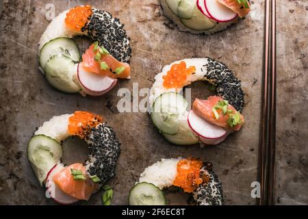 Sushi-Donuts mit Lachs, Gurke und Rettich auf dunklem Hintergrund, Draufsicht. Hybrid-Lebensmittel. Stockfoto