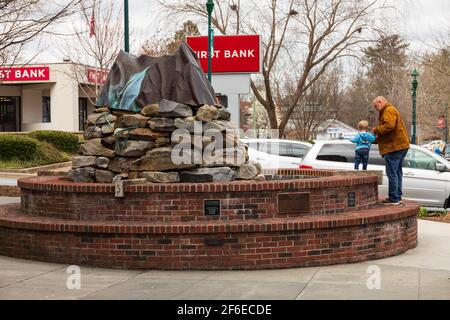 HENDERSONVILLE, NC, USA--23 MÄRZ 2021: Ein Vater mit einem kleinen Kind genießt am frühen Frühlingstag eine Bude auf dem Bürgersteig. Skulptur heißt Mountain Memory. Stockfoto