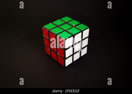 Avola, Italien - März 31st 2021: Nahaufnahme eines gelösten Rubik-Würfels auf schwarzem Hintergrund. Das Objekt zeigt seine roten, weißen und grünen Gesichter. Es war invente Stockfoto