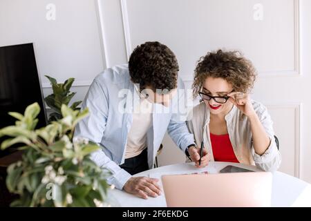 Freundliche Angestellte und Angestellte, die gemeinsam an einem Finanzbericht arbeiten, am Schreibtisch im modernen Büro sitzen und einen Laptop benutzen. Schöne Geschäftsfrau Stockfoto