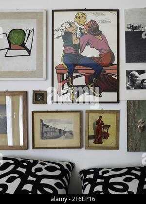Künstlerisches Schlafzimmer in einem Loft-Haus in Mailand, Italien. Detail der Wand hinter dem Bett mit mehreren gerahmten Kunstwerken und Drucken und Bildern Stockfoto