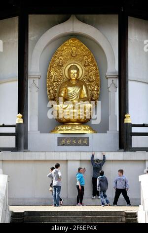 Kinder hängen mit dem Buddha. Eine vergoldete Bronzeskulptur des Buddha in der Friedenspagode, Battersea Park, London. Stockfoto