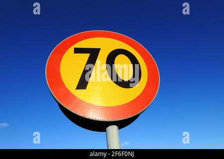 Low-Angle-Ansicht des kreisförmigen gelben 70 Geschwindigkeitsbegrenzungsfahrbahnschildes mit einer roten Grenze gegen einen blauen Himmel. Stockfoto