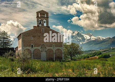 Die Kirche Santa Maria in Ronzano mit ihren Backsteinmauern und blinden Steinbögen. Im Hintergrund die Kette des Gran Sasso mit Schnee. Abruzzen Stockfoto