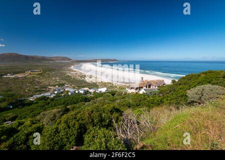 Panoramablick auf Noordhoek Long Beach mit weißem Sand in der Nähe von Kapstadt, Südafrika gegen blauen Himmel. Vom Chapmans Peak Drive aus gesehen. Die Stadt Kommet Stockfoto