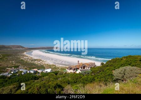 Panoramablick auf Noordhoek Long Beach mit weißem Sand in der Nähe von Kapstadt, Südafrika gegen blauen Himmel. Vom Chapmans Peak Drive aus gesehen. Die Stadt Kommet Stockfoto