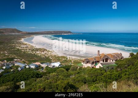 Panoramablick auf Noordhoek Long Beach mit weißem Sand in der Nähe von Kapstadt, Südafrika gegen blauen Himmel. Vom Chapmans Peak Drive aus gesehen. Die Stadt Kommet Stockfoto