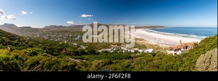 Panoramablick auf Noordhoek Long Beach mit weißem Sand in der Nähe von Kapstadt, Südafrika gegen blauen Himmel. Vom Chapmans Peak Drive aus gesehen. Die Stadt Kommet Stockfoto