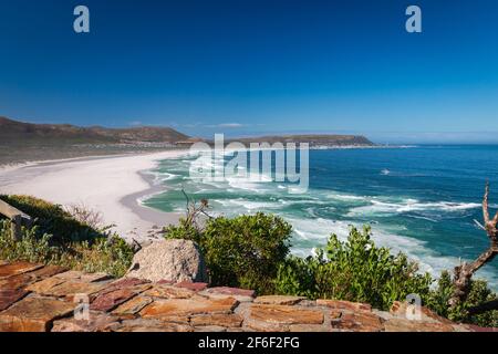 Panoramablick auf Noordhoek Long Beach mit weißem Sand in der Nähe von Kapstadt, Südafrika gegen blauen Himmel. Vom Chapmans Peak Drive aus gesehen. Die Stadt Kommet Stockfoto