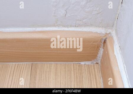 Nahaufnahme der zerbrochenen Fußböden an der Ecke des Wohnzimmers, die Farbe an der Wand hat sich aufgrund der Feuchtigkeit aus dem Regen abgeblättert. Vorderansicht Stockfoto