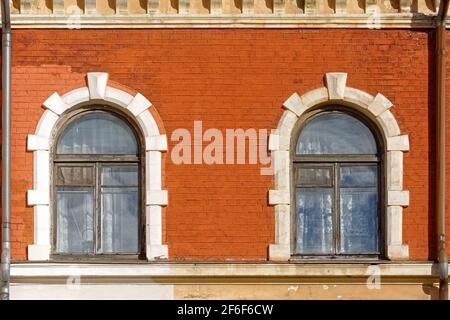 Zwei Bogenfenster mit alten Holzrahmen an einer alten roten Ziegelwand. Aus den Fenstern der Welt-Serie. Stockfoto
