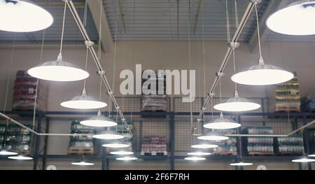 Nahaufnahme von glühenden Lampen in einem Lagerhaus mit Waren in den Regalen. Stockfoto