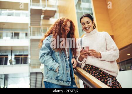 Mädchen, das einem Freund ihr Mobiltelefon zeigt, während sie auf der Treppe auf dem College-Campus nach unten geht. Zwei College-Mädchen, die aus der Klasse zurückkehren und ein Handy benutzen Stockfoto