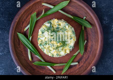 Gesunder Salat aus grünem Wildlech, pochiertem Ei und saurer Rahm auf dem Teller, Nahaufnahme. Salat mit wildem Knoblauch und gekochten Eiern Stockfoto