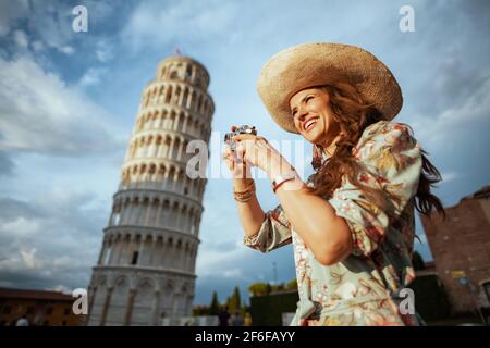 Happy moderne Solo-Tourist Frau in Blumenkleid mit Filmkamera und Hut in der Nähe Schiefen Turm in Pisa, Italien. Stockfoto