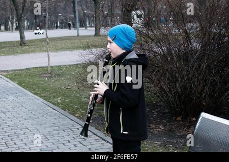 Dnepropetrovsk, Ukraine - 03.29.2021: Ein Junge im Park spielt Klarinette. Das Kind ist gut gelaunt. Stockfoto