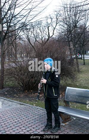 Dnepropetrovsk, Ukraine - 03.29.2021: Ein Junge im Park spielt Klarinette. Das Kind ist gut gelaunt. Stockfoto