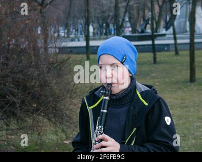 Dnepropetrovsk, Ukraine - 03.29.2021: Ein Junge im Park spielt Klarinette. Das Kind ist gut gelaunt. Stockfoto