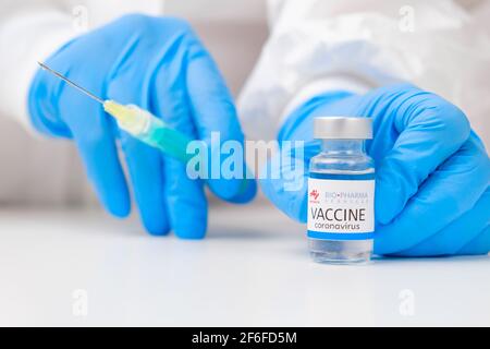 Bio Pharma-Impfstoff gegen Coronavirus und Spritze zur Injektion in die Hand von Gesundheitsarbeitern in Gummihandschuhen und Schutzanzug, März 2021, San Francisco Stockfoto